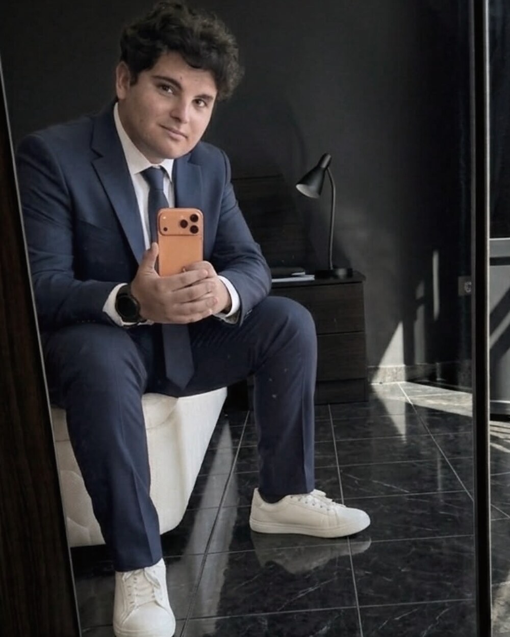 Aaron Alba, con traje, sentado frente a un espejo